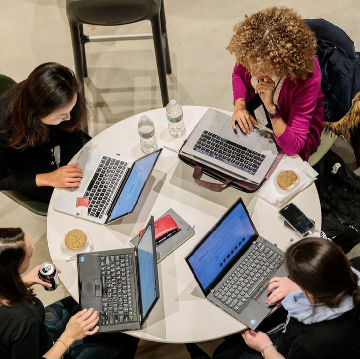 Four women sitting on a roundtable with their laptops open